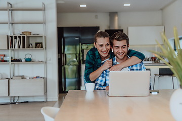 Image showing A young married couple is talking to parents, family and friends on a video call via a laptop while sitting in the living room of their modern house