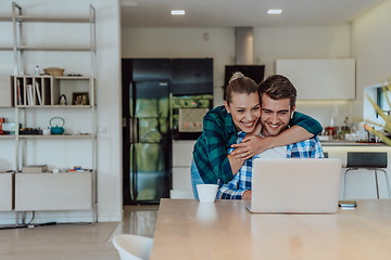 Image showing A young married couple is talking to parents, family and friends on a video call via a laptop while sitting in the living room of their modern house