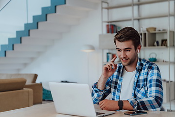 Image showing The man sitting at a table in a modern living room, with headphones using a laptop for business video chat, conversation with friends and entertainment