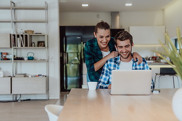 Image showing A young married couple is talking to parents, family and friends on a video call via a laptop while sitting in the living room of their modern house