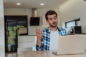 Image showing The man sitting at a table in a modern living room, with headphones using a laptop for business video chat, conversation with friends and entertainment