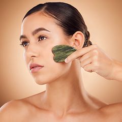 Image showing Beauty, gua sha and face of woman for skincare, facial treatment and wellness with spa stone. Salon, dermatology and girl on brown background with cosmetics, face massage and luxury tools in studio