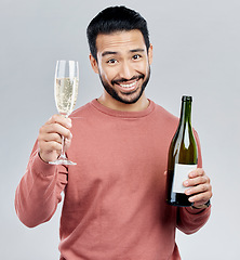 Image showing Portrait, champagne and toast with a man in studio on a gray background holding a bottle for celebration. Glass, alcohol and cheers with a handsome young man celebrating the new year tradition