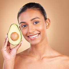 Image showing Portrait, skincare and avocado with a model woman in studio on a brown background for natural treatment. Face, food or antioxidants with an attractive young female holding healthy fruit for nutrition