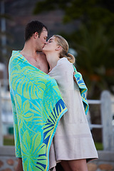 Image showing Sea, kiss and young couple in beach towels with love and bonding after engagement outdoor. Vacation travel, trust and happiness of a woman and man together by a ocean in nature sharing a sweet moment