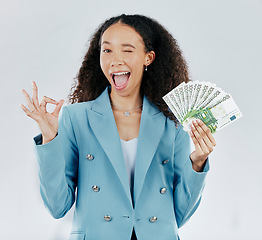 Image showing Portrait, wink and cash with a business woman in studio on a gray background making a perfect hand gesture. Funny face, finance and money with a female employee holding euro bills for investment