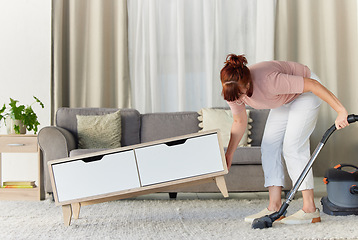 Image showing Woman, vacuum and housekeeping on carpet in living room for spring cleaning service, dust or dirt removal at home. Female cleaner lifting table and vacuuming for clean rug, mat or floor in the lounge