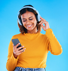 Image showing Happy woman, music headphones and phone in studio, blue background and happiness. Female model, smile and mobile for audio, streaming online radio and listening to podcast sound on media subscription