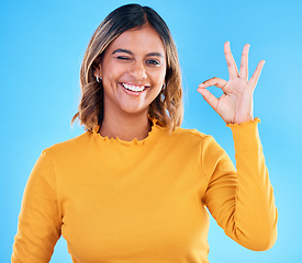 Image showing Ok, portrait and happy woman wink on blue background, studio and agreement of support. Female model, smile and okay hands of success, yes and winner of perfect emoji, thank you and review approval