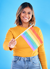 Image showing Portrait, flag and gay pride with a woman on a blue background in studio feeling proud of her lgbt status. Smile, freedom and equality with a happy young female holding a symbol of inclusion