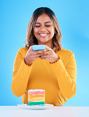 Image showing Woman, cake and studio with a phone for social media picture with a smile and excited to eat. Happy female person on blue background with rainbow color dessert for birthday or influencer celebration