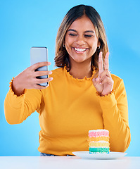 Image showing Woman, cake and peace selfie in studio for social media with a smile and excited to eat. Happy, female person and hand emoji on blue background with rainbow color dessert for birthday celebration