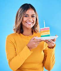 Image showing Birthday cake, happy portrait and woman in studio, blue background or party celebration. Female model, rainbow dessert and candle of special event, sweets or smile to celebrate happiness, wish or fun