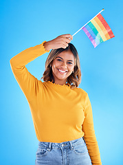 Image showing Portrait, rainbow flag and gay pride with a woman on a blue background in studio feeling proud of her lgbt status. Smile, freedom and equality with a happy young female holding a symbol of inclusion