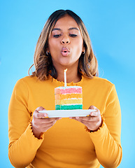 Image showing Birthday cake, woman and blow candles in studio, blue background and celebration. Female model, dessert and wishing at party, flame and special event, rainbow treat or celebrate happiness on backdrop