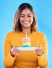 Image showing Birthday cake, happy party and woman in studio, blue background and celebration. Female model, rainbow dessert and candle of special event, sweets and smile to celebrate happiness, wish and surprise