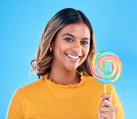 Image showing Portrait, lollipop and a woman on a blue background in studio wearing heart glasses for fashion. Smile, candy and sweet with an attractive young female eating a giant snack while feeling happy