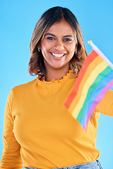 Image showing Portrait, flag and gay with a woman on a blue background in studio feeling proud of her lgbt status. Smile, freedom and equality with a happy young female holding a rainbow symbol of inclusion