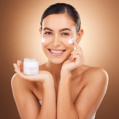 Image showing Portrait, skincare and lotion with a model woman in studio on a brown background for beauty or hydration. Face, skin and cream with a happy young female holding a container to apply moisturizer