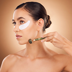 Image showing Woman beauty, eye patch and face roller for studio dermatology, healthcare or skincare treatment. Facial massage product, dermatology or female model with hyaluronic acid mask on brown background