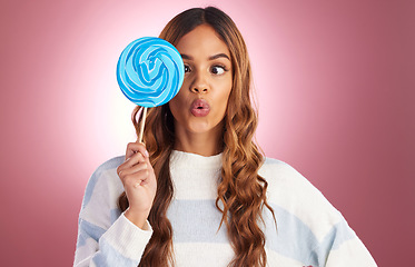 Image showing Portrait, funny face and lollipop with a woman on a pink background in studio holding giant candy. Comic, comedy and sweet with a playful young female feeling silly while eating a blue sugar treat
