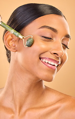 Image showing Woman, face and beauty, roller and skincare, smile and facial massage on studio background. Jade quartz cosmetic tools, dermatology and skin glow, happy Indian female and self care with cosmetics