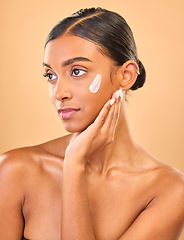 Image showing Face, beauty skincare and woman with cream in studio isolated on a brown background. Dermatology, cosmetics idea and thinking Indian female model with lotion, creme or moisturizer for skin health.