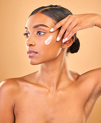 Image showing Face, skincare idea and woman with cream in studio isolated on a brown background. Dermatology, cosmetics and thinking Indian female model with lotion, beauty creme or moisturizer for skin health.