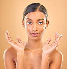 Image showing Face portrait, skincare and woman with cream in studio isolated on a brown background. Dermatology, cosmetics and serious Indian female model apply lotion, creme and moisturizer for healthy skin.