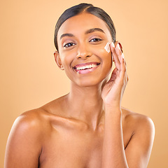 Image showing Face portrait, skincare and woman with cream in studio isolated on a brown background. Dermatology smile, cosmetics and happy Indian female model apply lotion, creme and moisturizer for healthy skin.