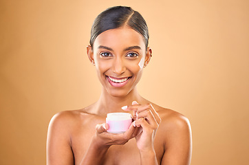 Image showing Face, skincare and woman with cream jar in studio isolated on a brown background. Dermatology cosmetics, portrait and happy Indian female apply lotion, creme and moisturizer product for healthy skin.