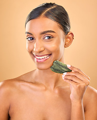 Image showing Face smile, skincare and woman with gua sha in studio isolated on a brown background. Dermatology portrait, massage and happy Indian female model with jade crystal or stone for healthy skin treatment