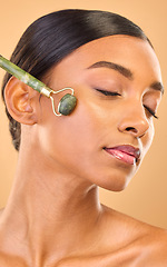 Image showing Face, skincare roller and woman with eyes closed in studio isolated on a brown background. Dermatology, facial massage and Indian female model with jade crystal for healthy skin treatment and beauty.