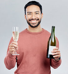 Image showing Portrait, champagne and cheers with a man in studio on a gray background holding a bottle for celebration. Glass, alcohol and toast with a handsome young man celebrating the new year tradition