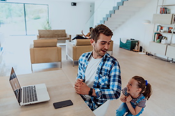 Image showing Work from home. Daughter interrupting her father while he is having a business online conversation on his laptop while sitting in modern living room