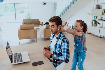 Image showing Work from home. Daughter interrupting her father while he is having a business online conversation on his laptop while sitting in modern living room