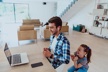 Image showing Work from home. Daughter interrupting her father while he is having a business online conversation on his laptop while sitting in modern living room