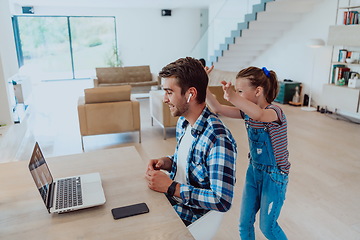 Image showing Work from home. Daughter interrupting her father while he is having a business online conversation on his laptop while sitting in modern living room