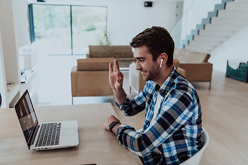 Image showing The man sitting at a table in a modern living room, with headphones using a laptop for business video chat, conversation with friends and entertainment