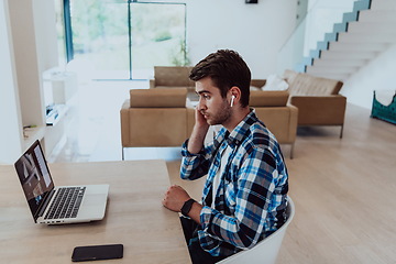 Image showing The man sitting at a table in a modern living room, with headphones using a laptop for business video chat, conversation with friends and entertainment