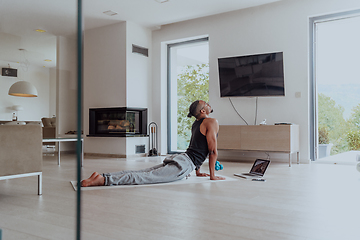 Image showing Training At Home. Sporty man doing training while watching online tutorial on laptop, exercising in living room, free space