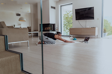 Image showing Training At Home. Sporty man doing training while watching online tutorial on laptop, exercising in living room, free space