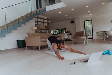 Image showing Training At Home. Sporty man doing training while watching online tutorial on laptop, exercising in living room, free space