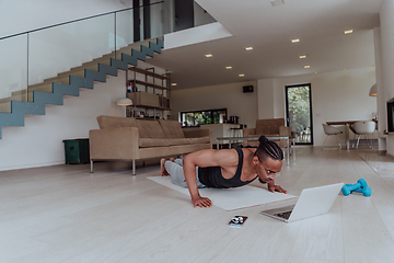 Image showing Training At Home. Sporty man doing training while watching online tutorial on laptop, exercising in living room, free space