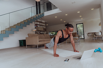 Image showing Training At Home. Sporty man doing training while watching online tutorial on laptop, exercising in living room, free space