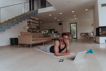 Image showing Training At Home. Sporty man doing training while watching online tutorial on laptop, exercising in living room, free space