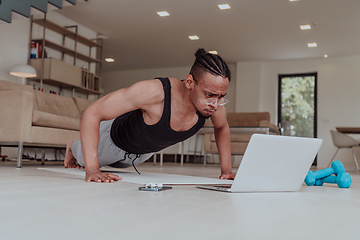 Image showing Training At Home. Sporty man doing training while watching online tutorial on laptop, exercising in living room, free space