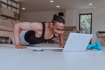 Image showing Training At Home. Sporty man doing training while watching online tutorial on laptop, exercising in living room, free space