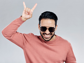 Image showing Portrait, rock on and hand gesture with a man in studio on a gray background feeling crazy or energetic. Face, rocker or hardcore and a male posing with a devil horns sign or symbol at a concert