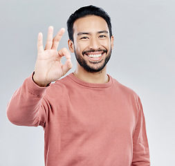 Image showing Hand, portrait and okay sign by man in studio with yes, vote or approval gesture against grey background. Finger, emoji and perfect symbol by asian male happy with decision, thank you or satisfied